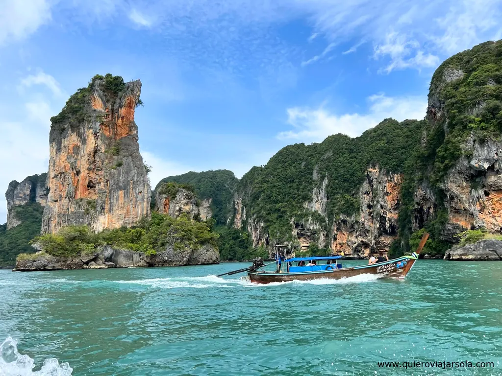 Un barco típico tailandés navegando por el mar frente a los acantilados de Railay Beach